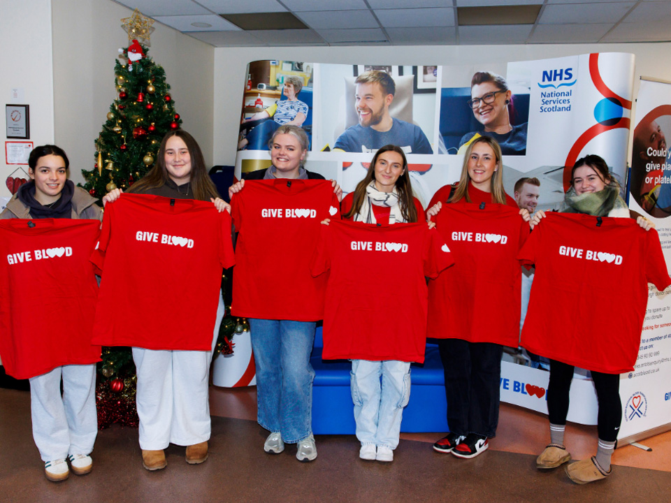Group of students holding red "Give Blood" t-shirts